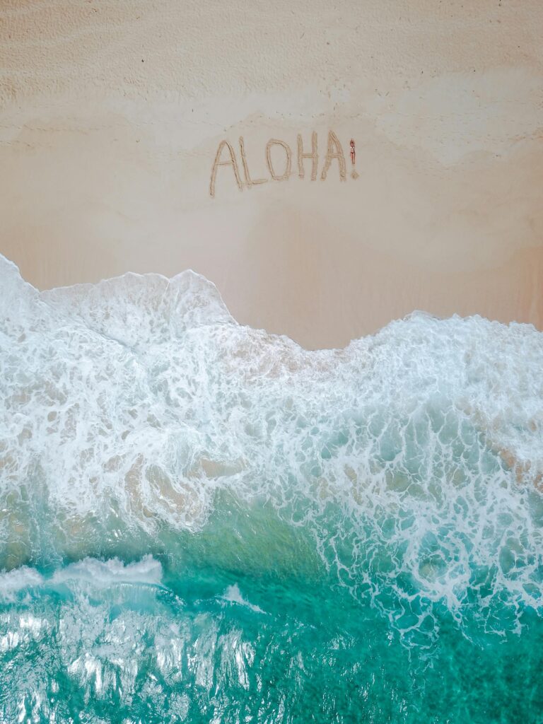 A serene aerial shot of a tropical beach with 'Aloha' written in the sand and waves crashing ashore.